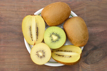 Plate with whole and cut fresh kiwis on wooden table, top view