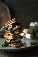 Delicious marshmallow sandwiches with crackers and chocolate on wooden table, closeup
