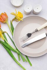 Composition with clean plate, crockery and beautiful flowers on white background
