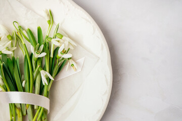 Plate with beautiful snowdrops and ribbon on white background