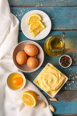 Bowl with tasty mayonnaise sauce and ingredients on color wooden background