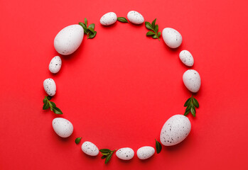 Frame made of Easter eggs and plant leaves on red background