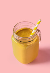 Mason jar of tasty yellow smoothie with straw on pink background