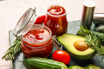 Jars with tasty ketchup and fresh vegetables on pink tile background