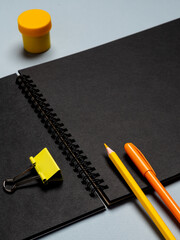Top view arrangement with notepad with  black  sheets and pens, pencils, paper clips and other office supplies on blue background