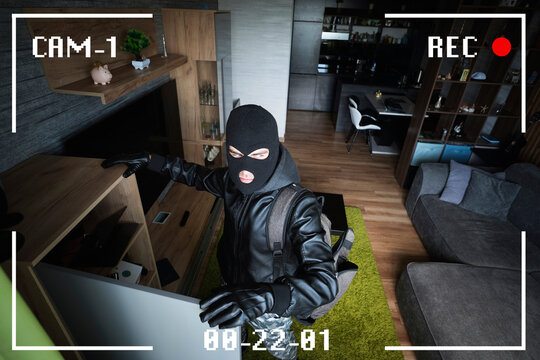 A man in a black mask is trying to rob a house. There is recording on an outdoor video surveillance camera. The robber noticed a security camera. Robbery of a private house. Criminal concept