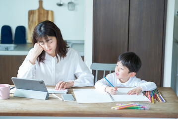 部屋で遊ぶ子供と、隣で仕事をして疲れた表情の母親