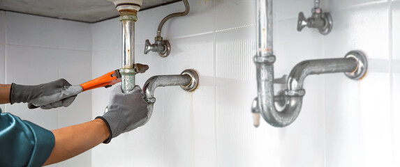 Technician plumber using a wrench to repair a water pipe under the sink. Concept of maintenance, fix water plumbing leaks, replace the kitchen sink drain, cleaning clogged pipes is dirty or rusty.