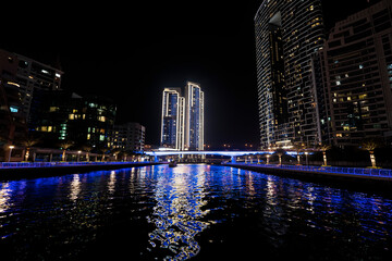 Fototapeta na wymiar view of footbridge with tourists leading to numerous skyscrapers with hotels and residential buildings on the Persian Gulf coast in Dubai at night