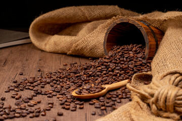 The many coffee beans are placed around on a wooden table in a warm, light atmosphere, on a dark background, with copy space.