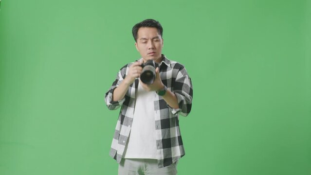 Asian Photographer Having A Neck Ache After Using A Camera Taking Some Pictures While Standing On Green Screen Background In The Studio
