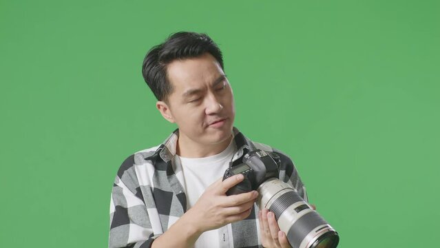 Close Up Of Asian Photographer Thinking About The Pictures Footage And Raising His Index Finger While Looking At The Pictures In The Camera On Green Screen Background In The Studio
