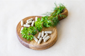 Vegetable capsules and sprigs of greens lie on a small wooden board, a concept of natural additives