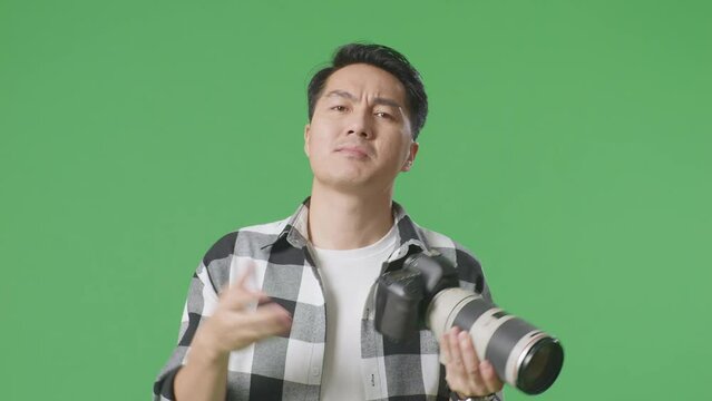Close Up Of Puzzled Asian Photographer Looking At The Pictures In The Camera, Saying Why And Making Gestures Doubtfully While Standing On Green Screen Background In The Studio
