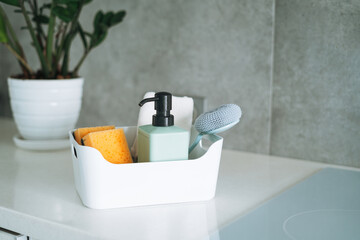 Kitchen cleaning supplies brush, liquid soap, dish sponge in container on kitchen counter at home