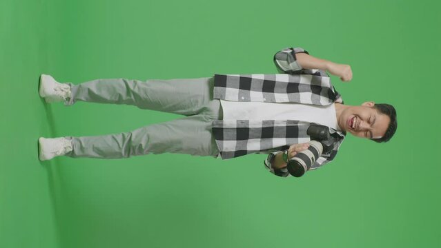 Full Body Of Asian Photographer Looking At The Pictures In The Camera Then Screaming Goal Celebrating Satisfied With The Result While Standing On Green Screen Background In The Studio
