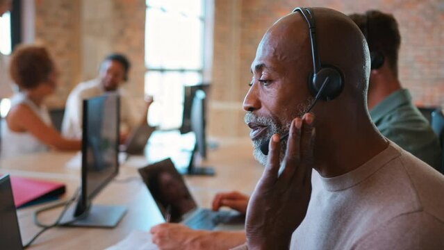 Portrait of mature businessman in multi-cultural business team wearing headsets in customer support centre - shot in slow motion