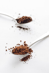 Heaped teaspoon of instant coffee with ground black coffee in the background
