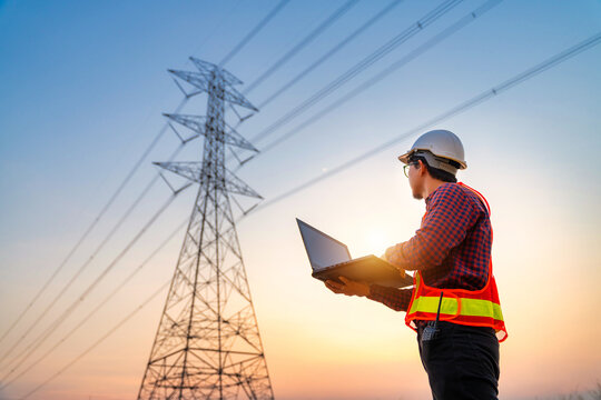 Asian electrical engineers checking location using a notebook computer standing at a power station to view the planning work by producing electrical energy at high voltage electrodes.