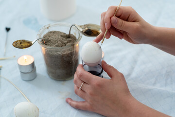 Female hands paint a white Easter egg with pattern according to Sorbian tradition with a needle...