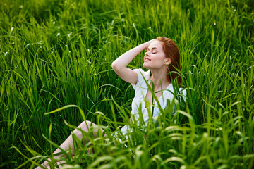 cute, happy woman sitting in tall grass on a sunny day in a light dress