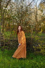 Naklejka premium an elegant, sophisticated woman poses relaxed standing near a wicker fence at the dacha in a long orange dress