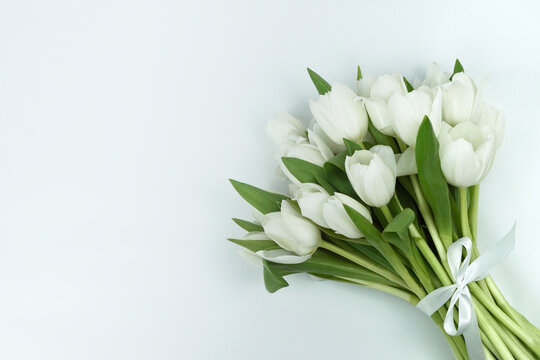 Liegender Blumenstrauß aus weißen Tulpen mit weißer Schleife rechts im Bild, weißer Hintergrund, links freier Platz, horizontal