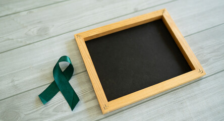 A dark green ribbon and a small black board, Concept related to medical awareness Selective focus