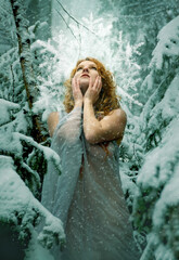 Fototapeta na wymiar Beautiful young sexy christmas redhead snow girl with a big snowcrystal, in winter nature in a long light delicate dress in a cold frosty winter forest, a frost fairy like a cute angel nymph