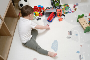 Toddler baby boy is playing cars sitting on a rug in the nursery. A small child is playing with...