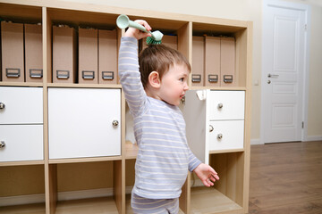 Happy toddler baby with a cleaning brush in the house. A funny child is holding a large brush in his hands.