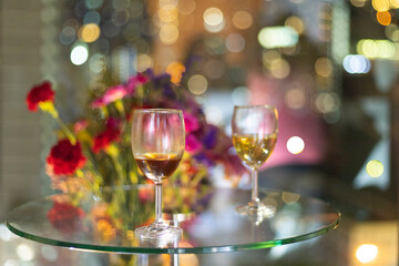 glass wine on table near window with blurred bokeh colorful City light and bunch of rose flowers in background.