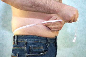 a man in jeans with a small belly measures the waist with a ribbon close-up - the concept of body positive