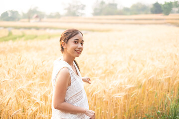 Fototapeta na wymiar Young Asian women in white dresses standing in the Barley rice field season golden color of the wheat plant at Chiang Mai Thailand