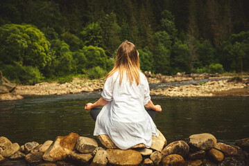 Woman doing yoga on the stone at the mountain river. Carpathians