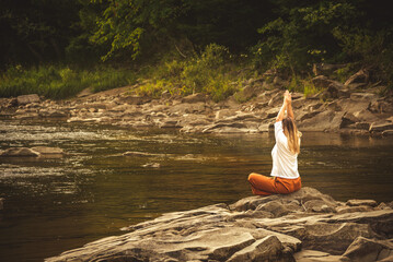 Woman doing yoga on the stone at the mountain river. Carpathians