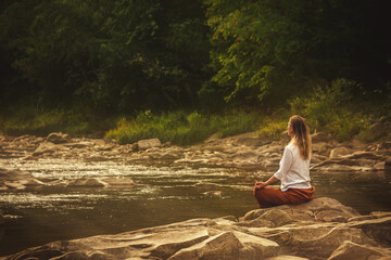 Woman doing yoga on the stone at the mountain river. Carpathians