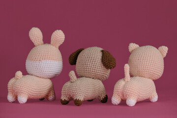 Amigurumi three pets dolls on pink background. DIY soft toys made of natural cotton and wool. Cute little kitten, puppy and rabbit crocheted, handmade art. Rear view.