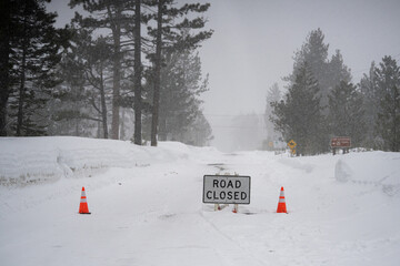 Road closed sign during winter storm with sign and red cones blocking road near Lake Tahoe.   Ideal for themes of winter weather, road safety, or natural hazards during winter storms.