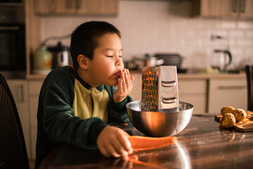 A little boy licks his fingers from carrot juice, helps his mother in the kitchen, cleans vegetables. Mother's Day, Women's Day