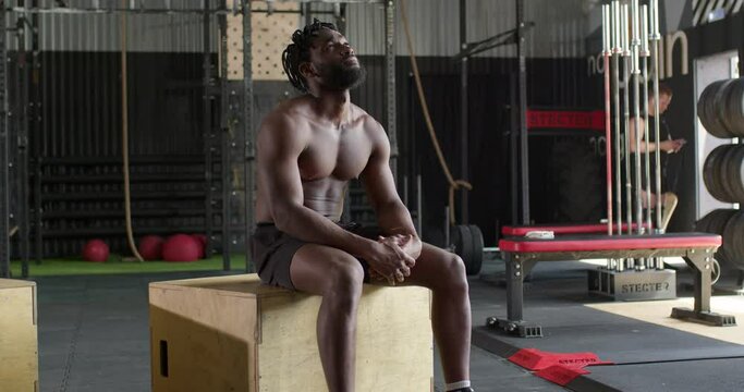 muscularpensive sweaty African man sitting on wooden box after cross fit workout Sportsman in black shorts has rest during training Tiredness bearded guy look up