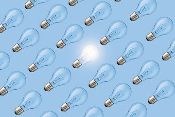 Creative fresh light bulb glowing among many extinguished bulbs on blue background, top view. Light...