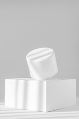 Mock up of white jar for packaging cosmetics on platform. Container with moisturizer without marking close-up on podium, in rays of sunlight. White background, vertical image. Concept of skin care