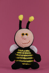 One bee black with yellow stripes and funny wings and horns crocheted, handmade art. Front view. Amigurumi bumblebee doll on pink background. Soft DIY toy made of cotton.