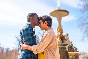 Couple of multi-ethnic men in a city fountain, lgbt concept, in a romantic pose kissing each other on the forehead