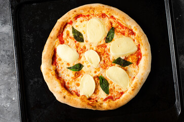 Frozen Italian Pizza Margherita with Mozzarella and Basil Leaves on Dark Background