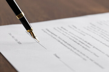 Writing on document with fountain pen at wooden table, closeup. Notary contract