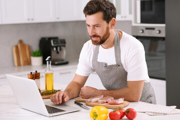 Fototapeta na wymiar Man making dinner while watching online cooking course via laptop in kitchen