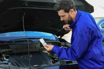 Worker checking motor oil level with dipstick outdoors