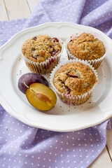 Seasonal muffins with plums and poppy seeds on white wooden and textile background close up selective focus 
